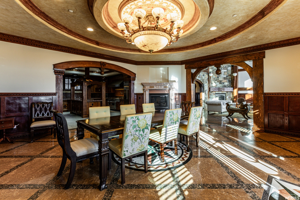 Tiled dining area with ornate columns, a tray ceiling, crown molding, and a chandelier