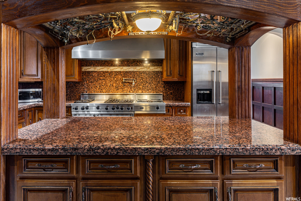 Kitchen featuring tasteful backsplash, dark stone countertops, stove, and stainless steel built in refrigerator