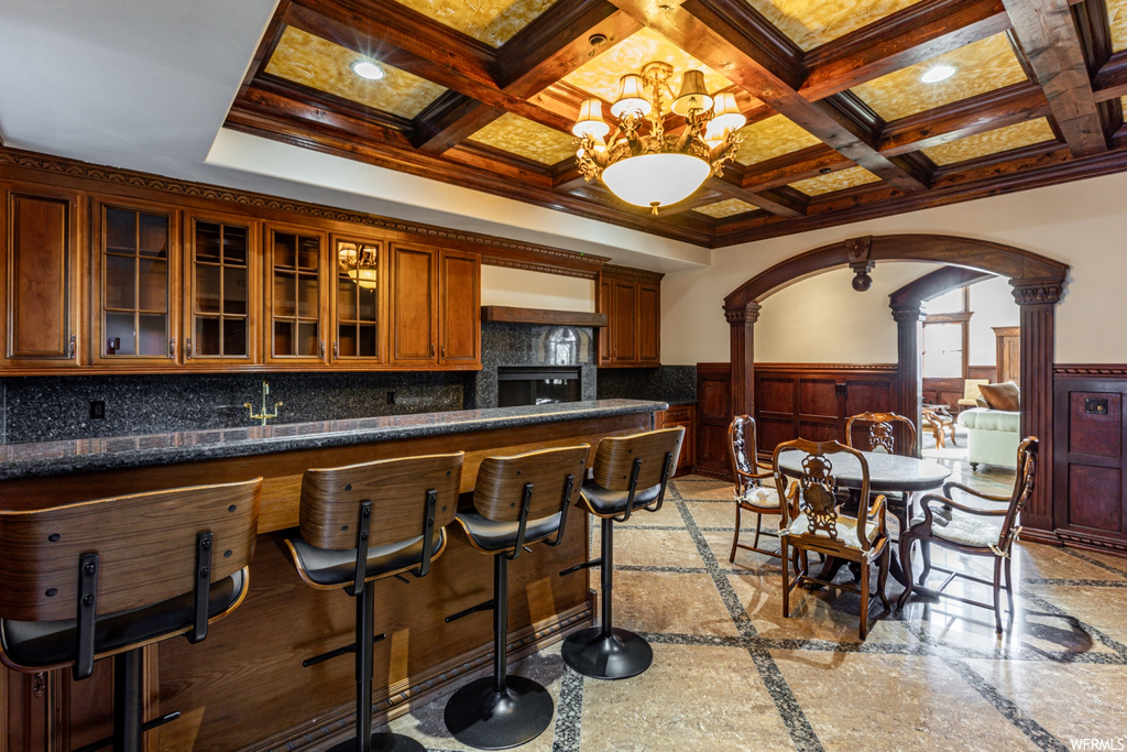 Kitchen with light tile flooring, a notable chandelier, a breakfast bar, backsplash, and coffered ceiling