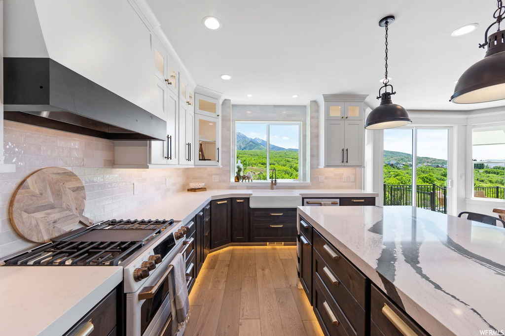 Kitchen featuring stainless steel finishes, gas range oven, exhaust hood, light hardwood flooring, dark brown cabinets, and light countertops