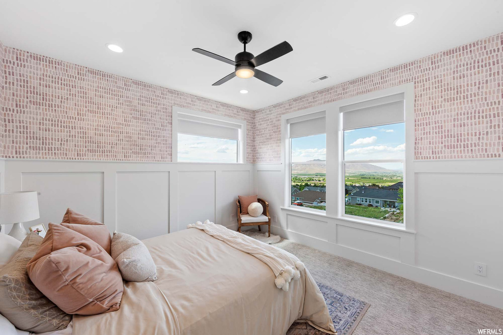 Carpeted bedroom with a ceiling fan and multiple windows