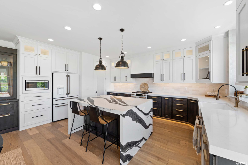 Kitchen with a center island, a kitchen bar, refrigerator, light parquet floors, light countertops, white cabinets, and pendant lighting