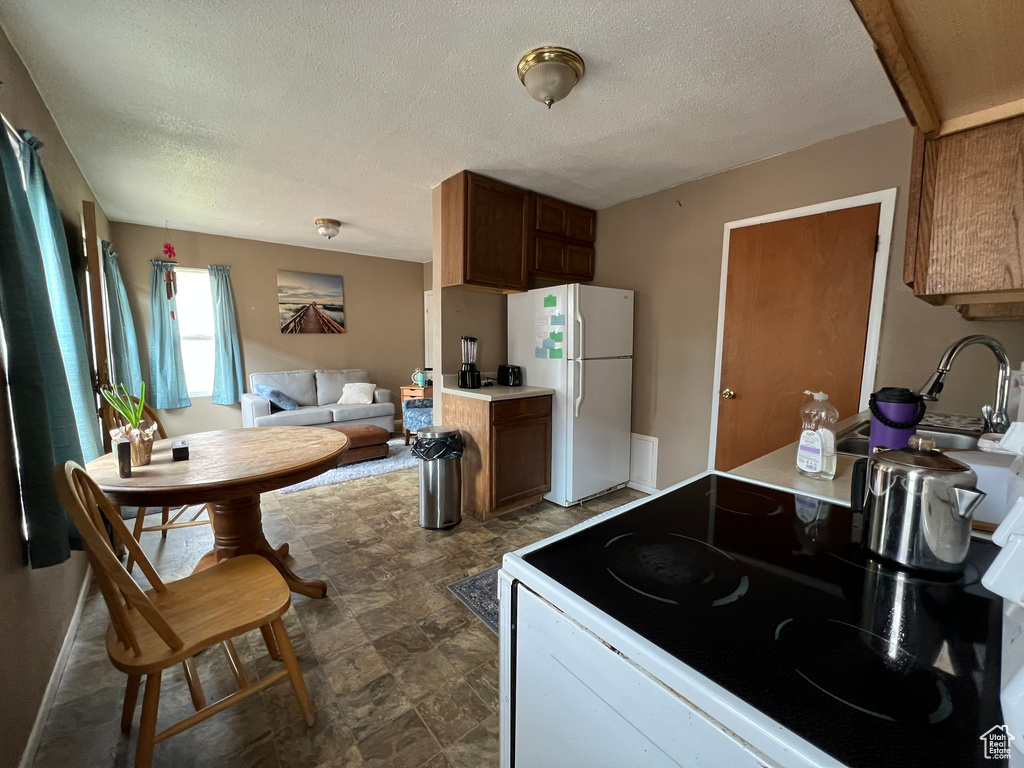 Kitchen with freestanding refrigerator, range with electric cooktop, a textured ceiling, stone finish flooring, and brown cabinetry