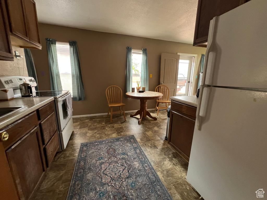 Kitchen featuring white appliances, a textured ceiling, dark brown cabinetry, light countertops, and baseboards