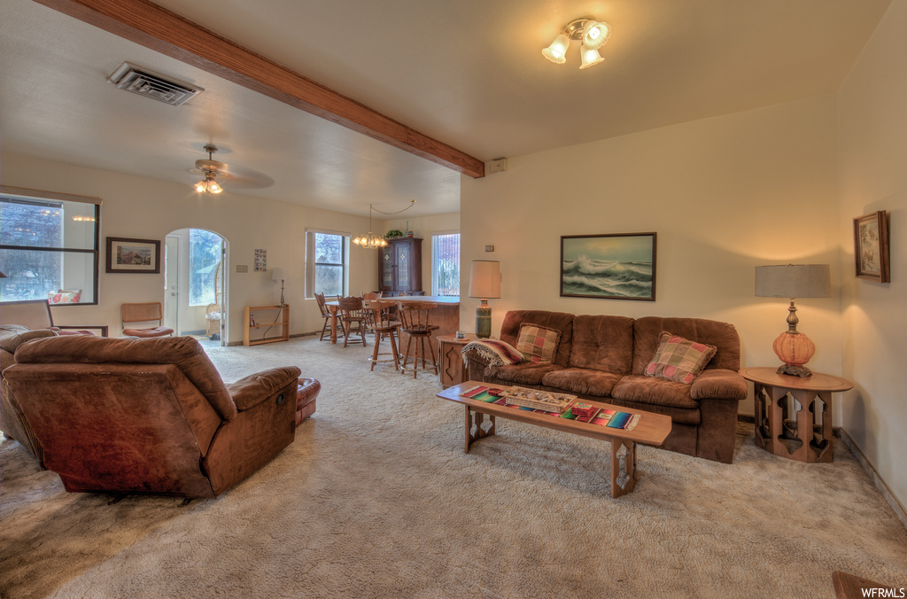Carpeted living room with a ceiling fan, wood beam ceiling, and a wealth of natural light
