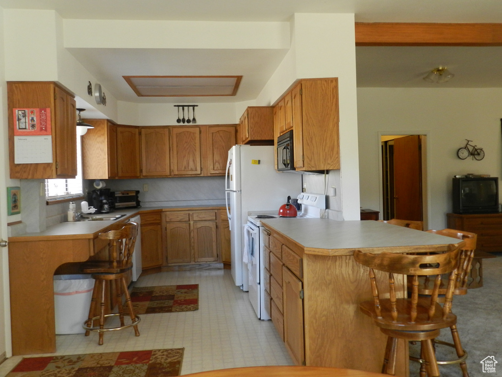 Kitchen with white appliances, a peninsula, a breakfast bar area, a sink, and brown cabinets