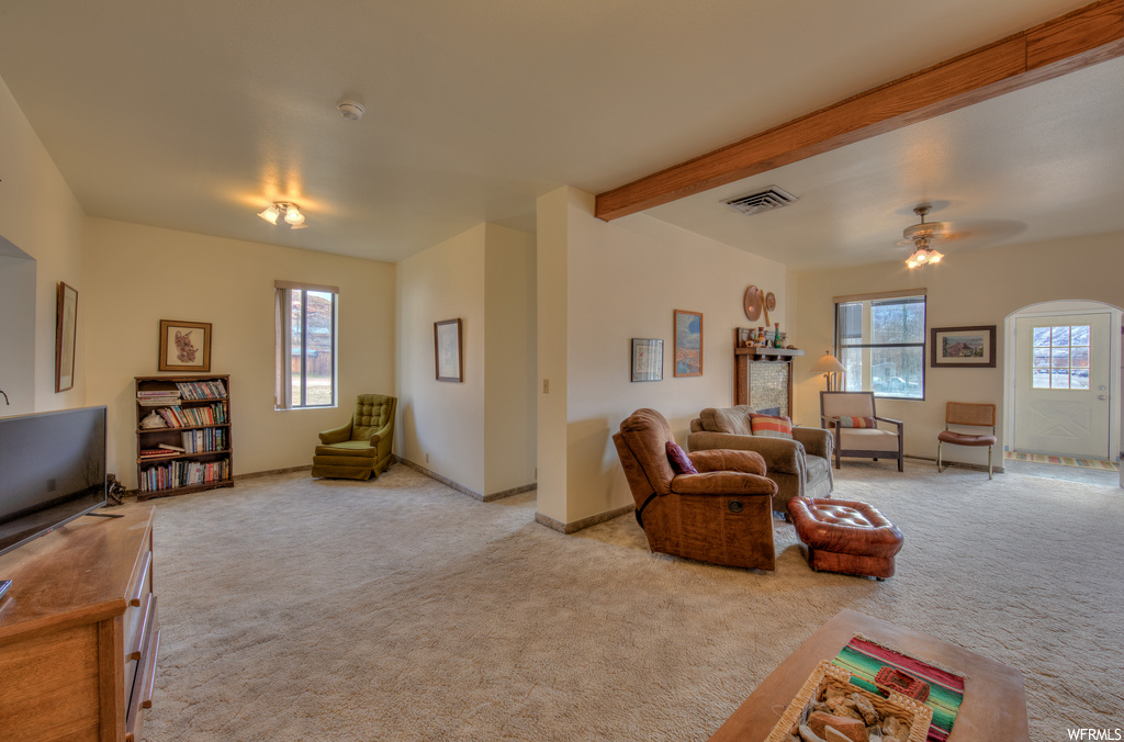 Living room featuring carpet, a ceiling fan, wood beam ceiling, natural light, and TV