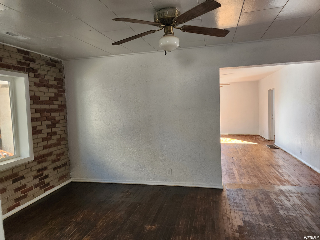 Unfurnished room featuring dark hardwood / wood-style flooring, ceiling fan, and brick wall