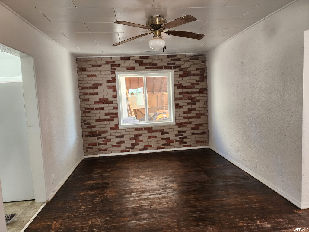 Empty room with ceiling fan, crown molding, dark wood-type flooring, and brick wall