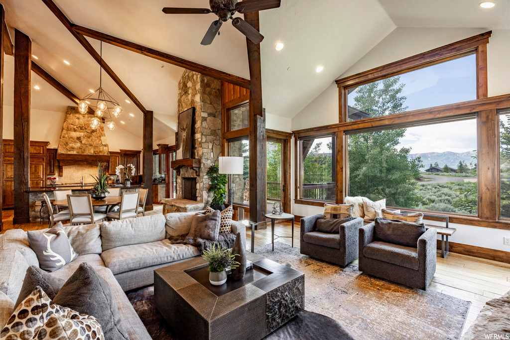 Hardwood floored living room featuring lofted ceiling with beams, a fireplace, a high ceiling, natural light, and a ceiling fan