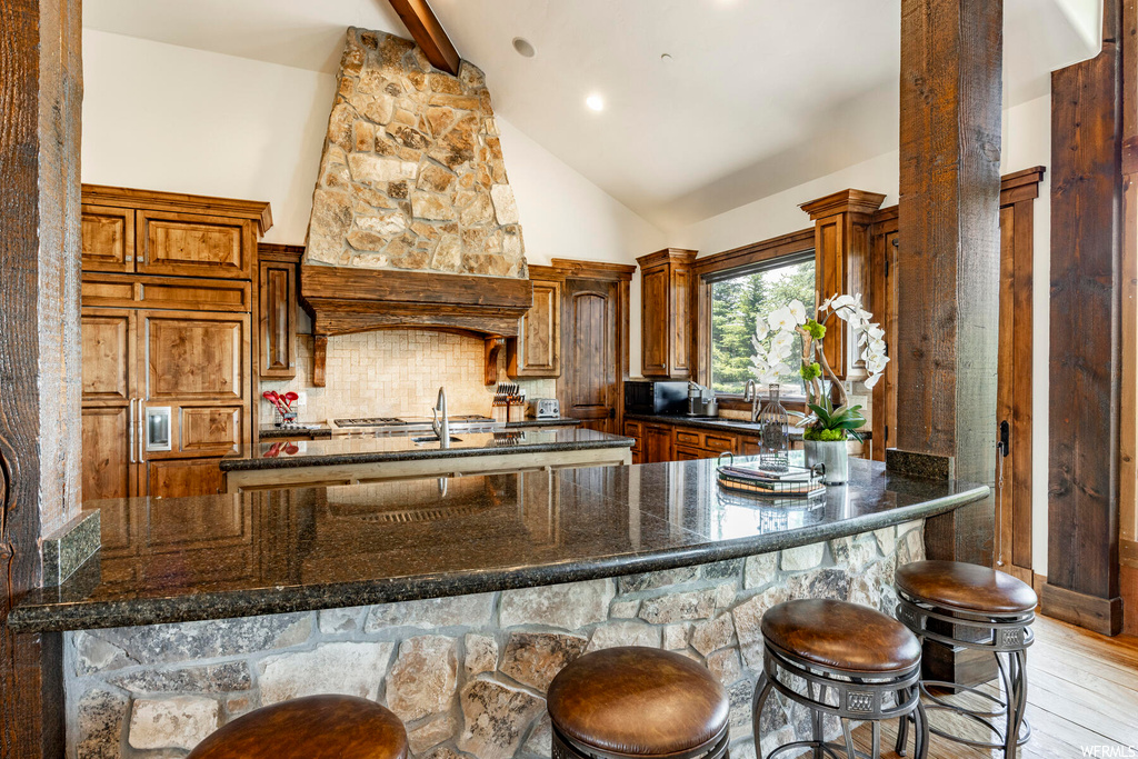 Kitchen featuring vaulted ceiling, a kitchen bar, and dark granite-like countertops