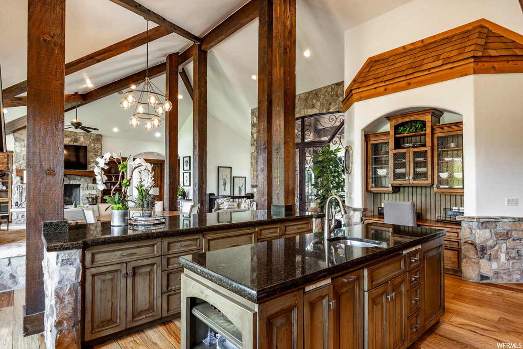 Kitchen featuring hardwood floors, natural light, a fireplace, a high ceiling, a center island, vaulted ceiling with beams, and dark stone countertops