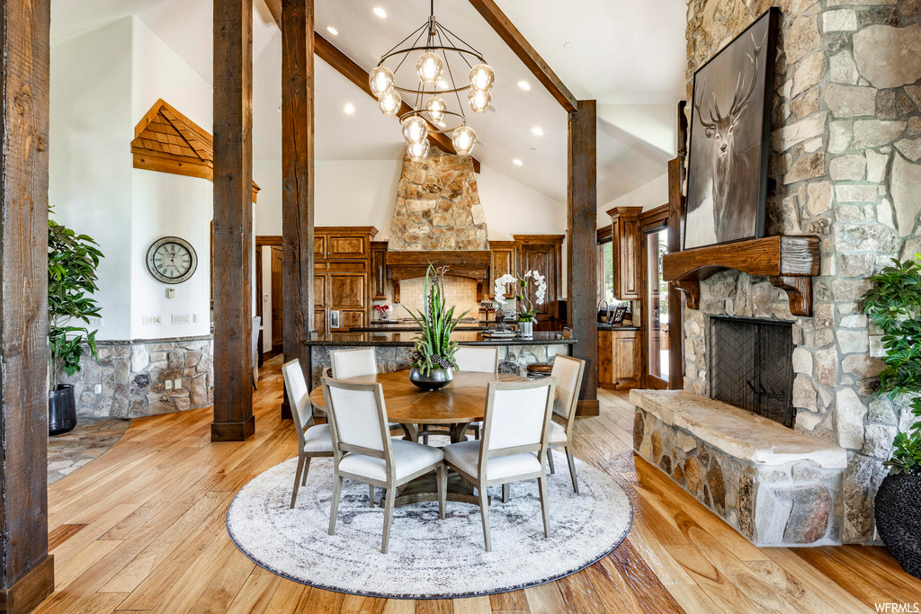 Dining area featuring hardwood floors, a fireplace, a high ceiling, a chandelier, and lofted ceiling with beams