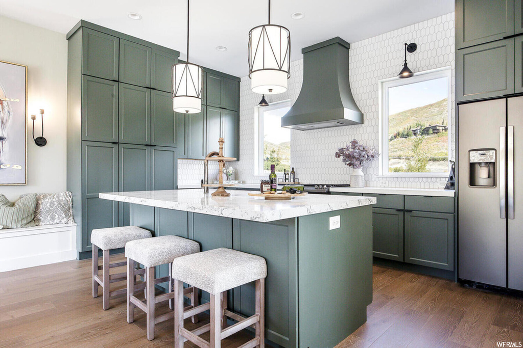 Kitchen with premium range hood, stainless steel fridge with ice dispenser, hanging light fixtures, dark hardwood / wood-style floors, and green cabinets