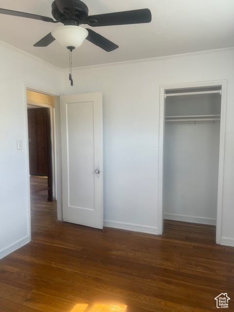 Unfurnished bedroom featuring dark wood-type flooring, a closet, ceiling fan, and crown molding
