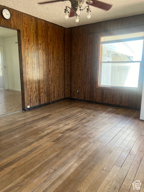 Empty room with wood walls, ceiling fan, hardwood / wood-style flooring, and a textured ceiling