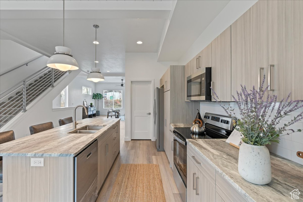 Kitchen with light hardwood / wood-style flooring, a kitchen island with sink, sink, decorative light fixtures, and appliances with stainless steel finishes