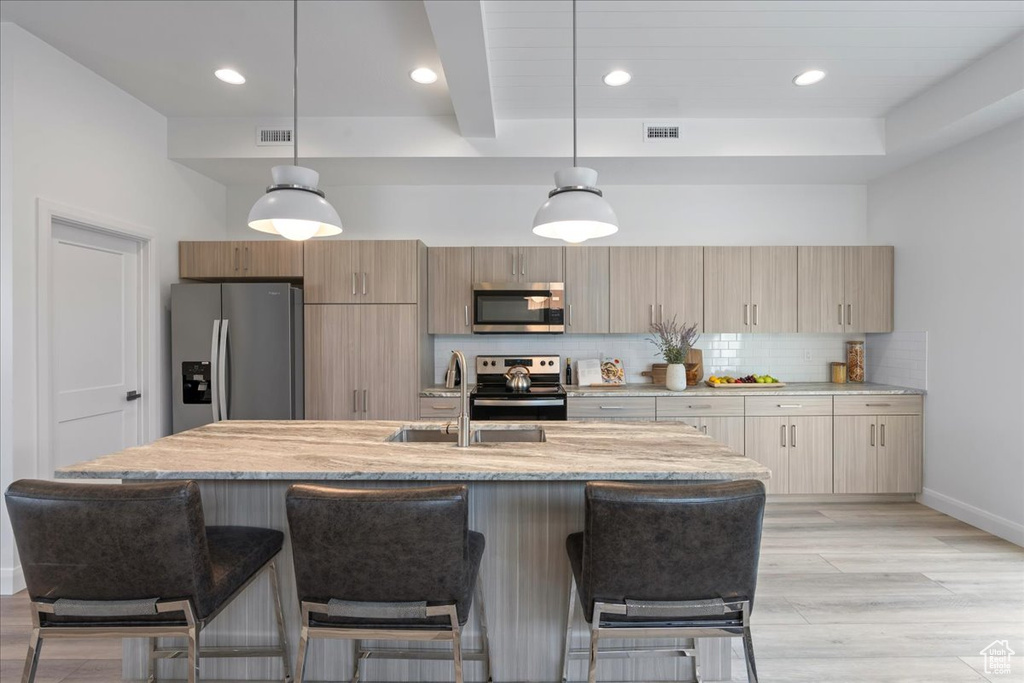 Kitchen featuring light stone counters, tasteful backsplash, appliances with stainless steel finishes, light hardwood / wood-style floors, and decorative light fixtures