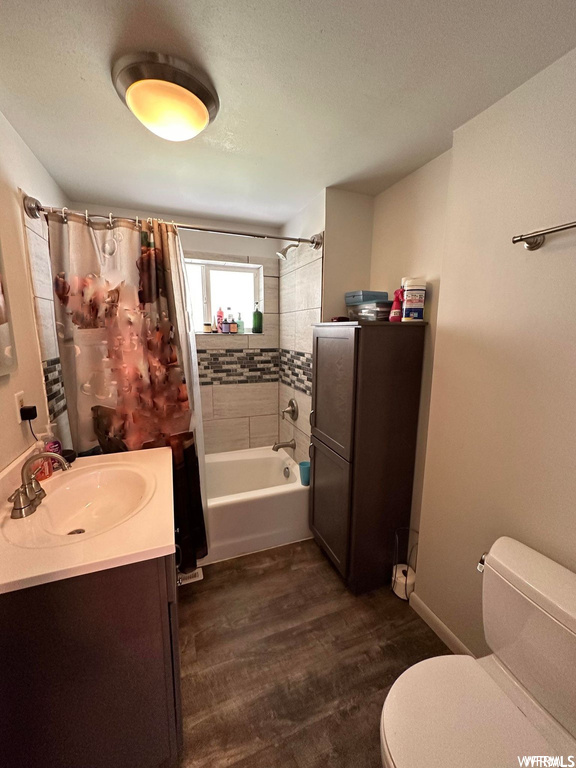 Full bathroom featuring hardwood flooring, shower / bath combination, toilet, shower curtain, and vanity