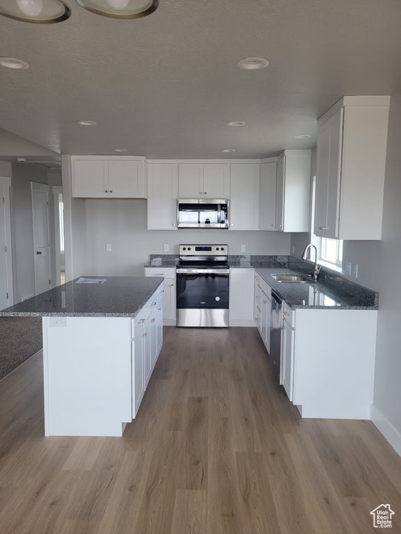 Kitchen featuring white cabinets, a center island, appliances with stainless steel finishes, and hardwood / wood-style floors