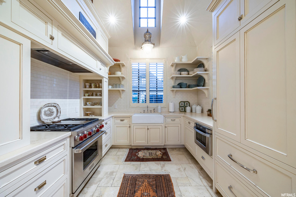 Kitchen featuring a wealth of natural light, stainless steel oven, gas range oven, light tile floors, white cabinetry, pendant lighting, and light countertops