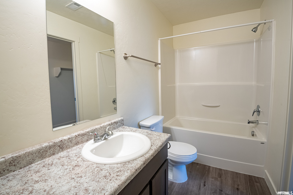 Full bathroom with hardwood floors, mirror, shower / tub combination, oversized vanity, and toilet
