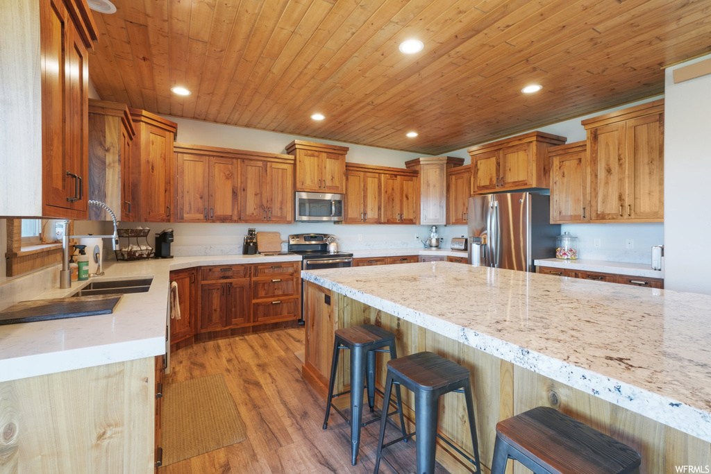 Kitchen with a breakfast bar area, refrigerator, stainless steel microwave, range oven, light granite-like countertops, light hardwood floors, and brown cabinetry