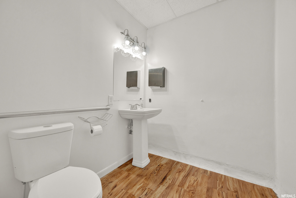 Half bathroom with hardwood flooring, washbasin, mirror, and toilet