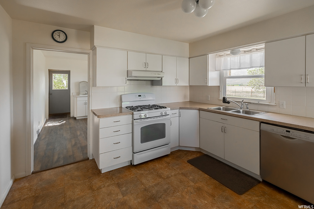 Kitchen with natural light, extractor fan, gas range oven, dishwasher, light countertops, white cabinets, and dark flooring