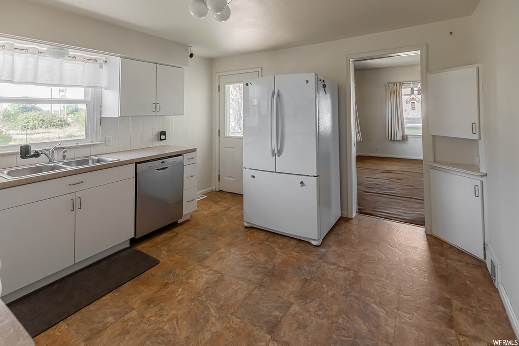 Kitchen featuring a wealth of natural light, dishwasher, refrigerator, dark floors, and white cabinetry