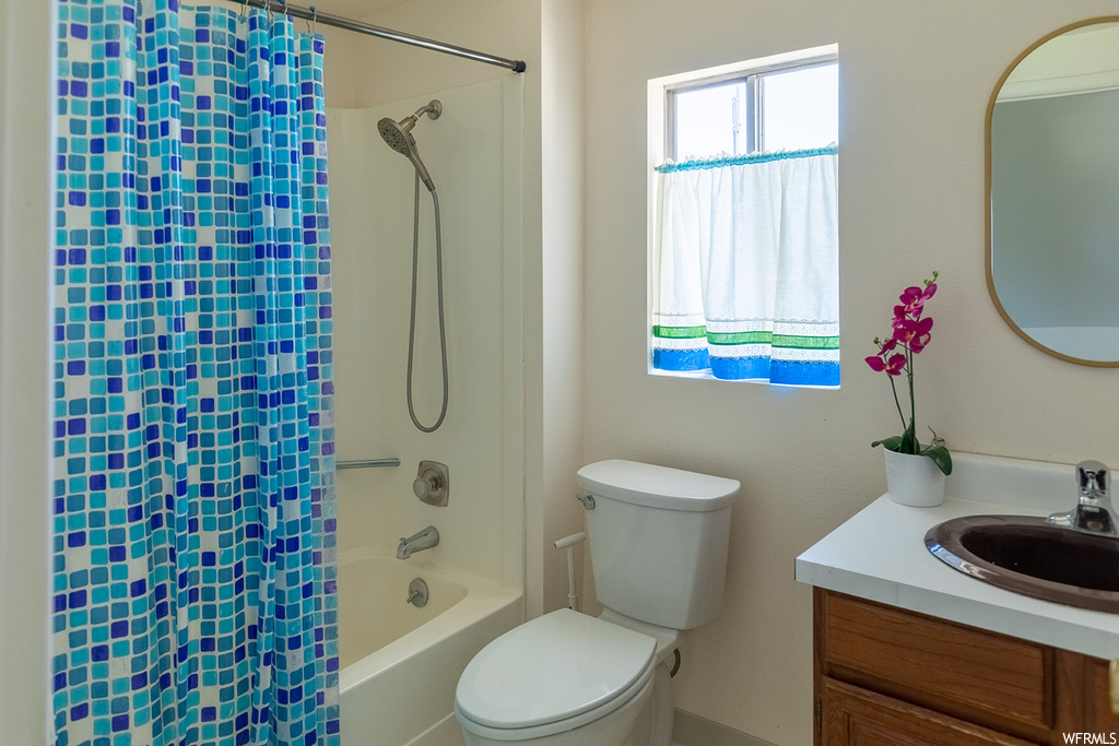 Full bathroom featuring natural light, shower / bathtub combination, mirror, vanity with extensive cabinet space, shower curtain, and toilet