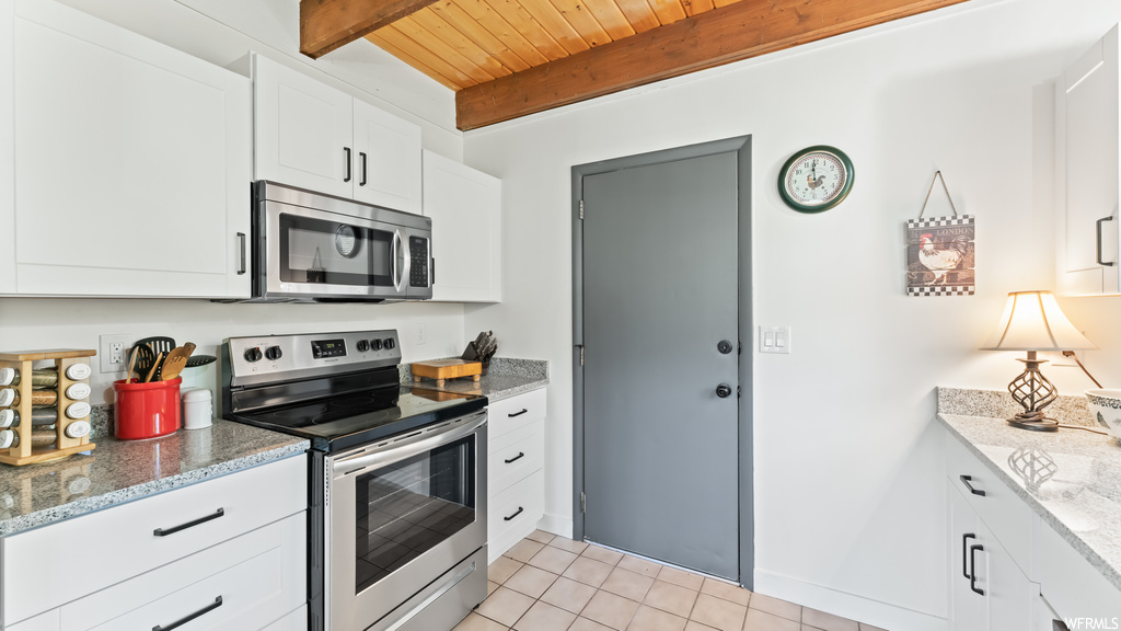 Kitchen featuring wood beam ceiling, microwave, electric range oven, light countertops, white cabinets, and light tile floors