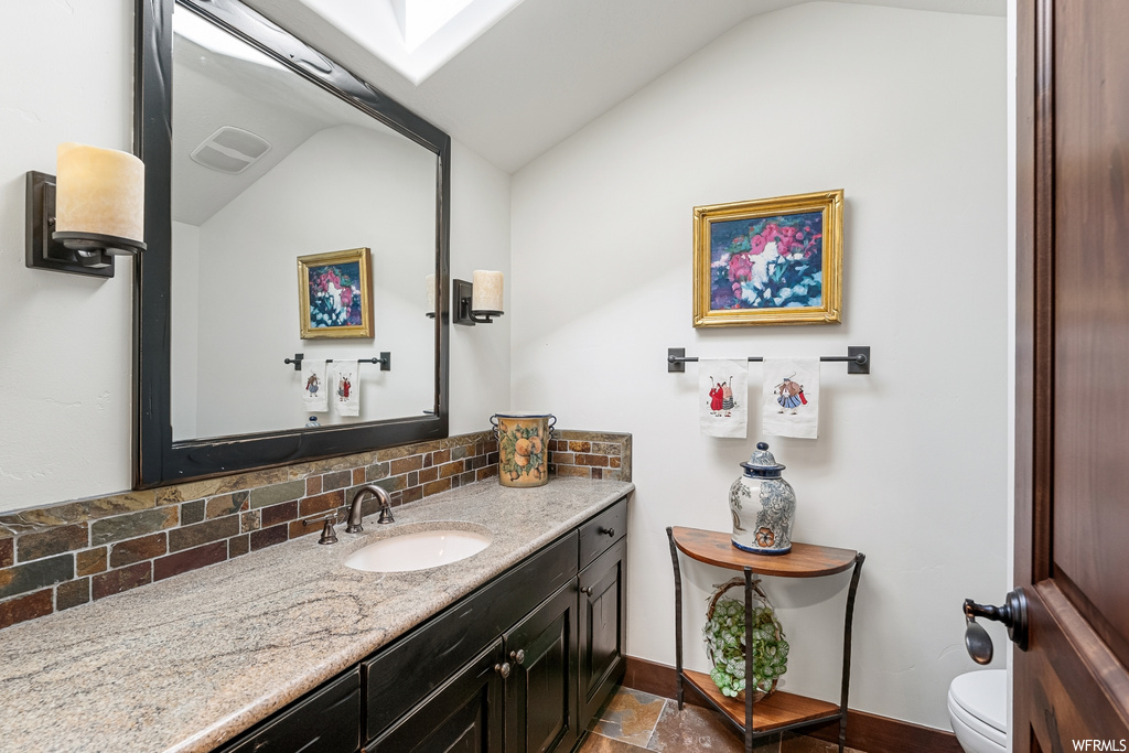Half bath featuring vaulted ceiling, mirror, vanity with extensive cabinet space, and toilet