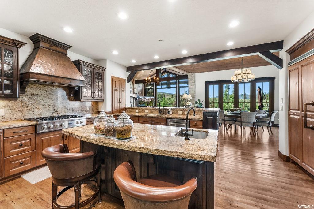 Kitchen with a breakfast bar area, a kitchen island, natural light, dishwasher, extractor fan, gas stovetop, light granite-like countertops, and light hardwood flooring