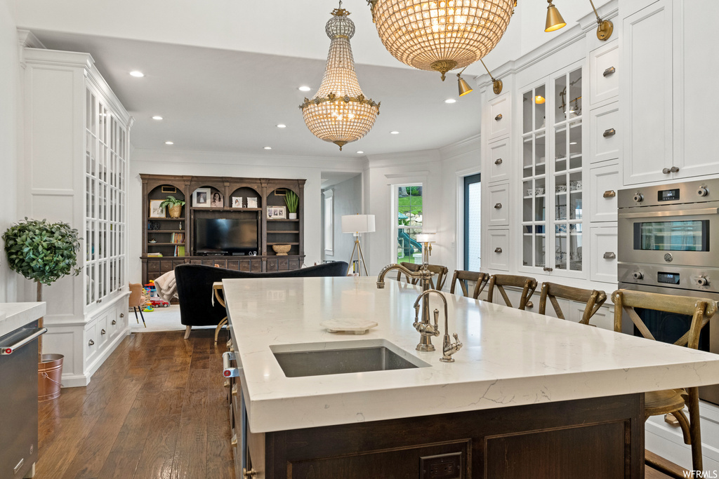 Kitchen featuring a breakfast bar, natural light, a notable chandelier, TV, oven, light countertops, and a center island with sink