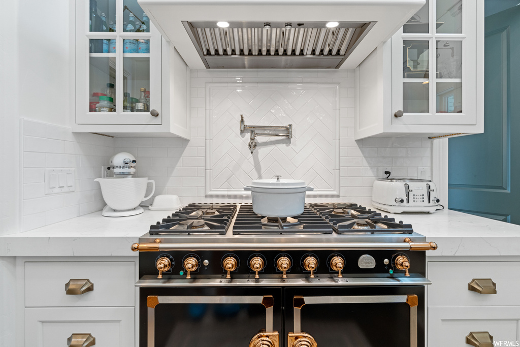 Kitchen featuring ventilation hood, gas range oven, stainless steel finishes, and white cabinetry
