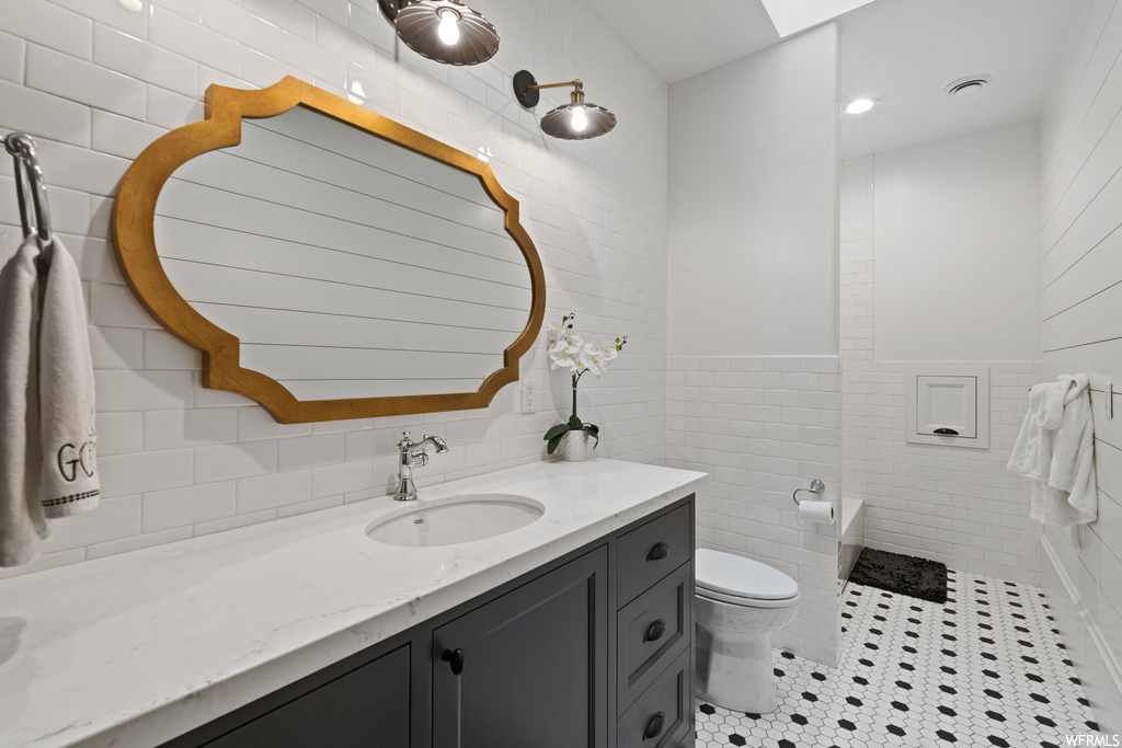 Half bath with tile flooring, multiple mirrors, toilet, and vanity
