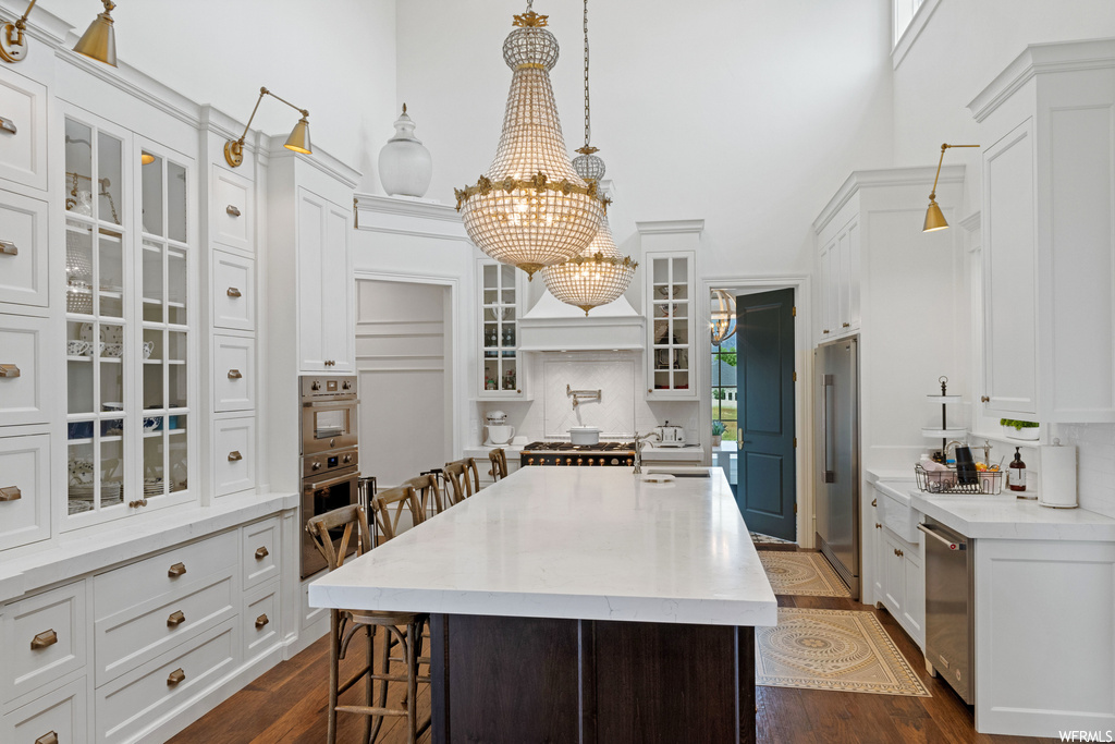 Kitchen with a kitchen island, a notable chandelier, hardwood floors, dishwasher, oven, light countertops, and pendant lighting