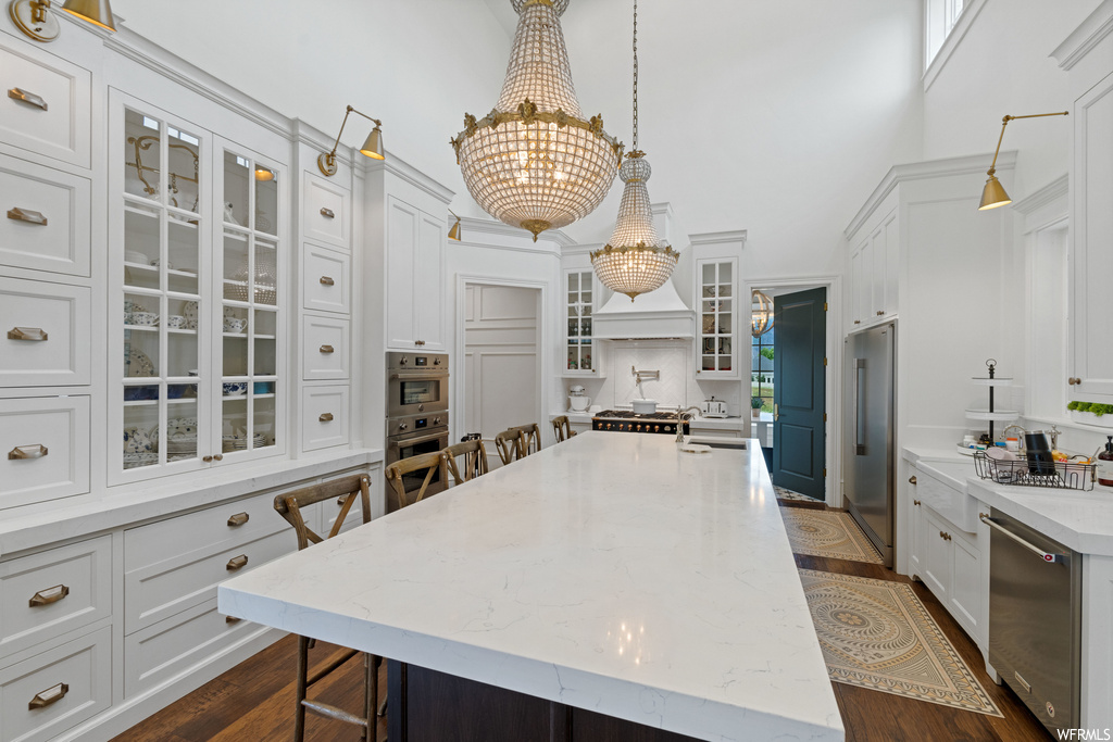 Kitchen with a kitchen island, hardwood floors, a notable chandelier, double oven, light countertops, pendant lighting, and white cabinetry