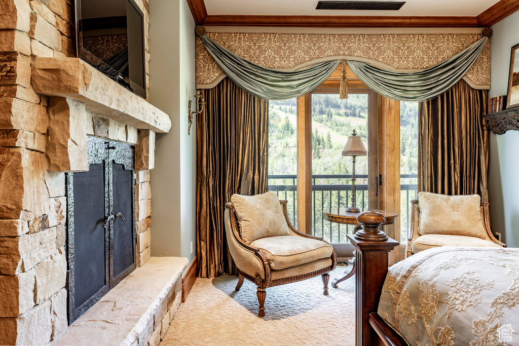 Bedroom with crown molding, light carpet, a stone fireplace, and access to exterior