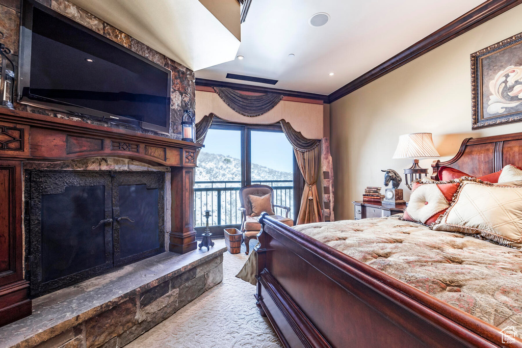 Bedroom with ornamental molding, light carpet, a stone fireplace, and access to exterior