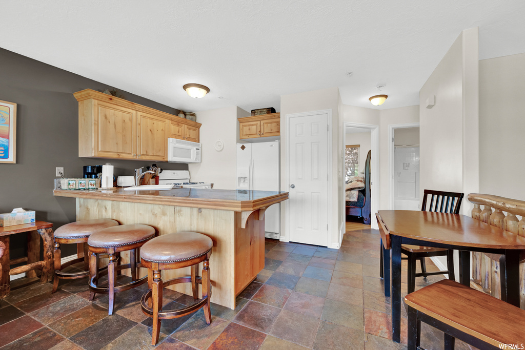 Kitchen with a breakfast bar area, tile flooring, range oven, microwave, light countertops, and brown cabinets