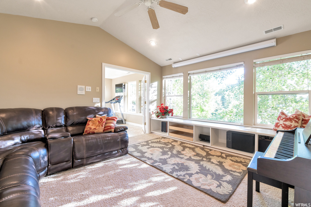 Carpeted living room featuring natural light, lofted ceiling, and a ceiling fan