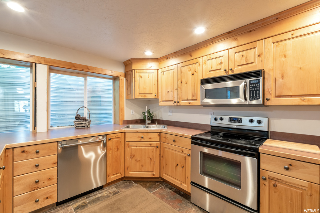 Kitchen featuring microwave, electric range oven, stainless steel dishwasher, brown cabinets, and light countertops