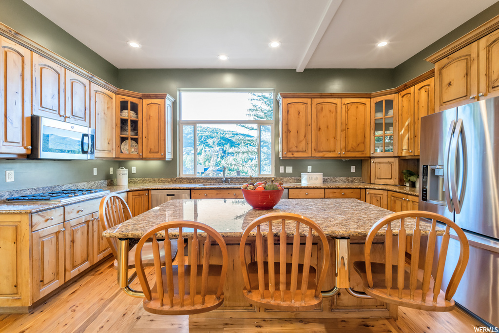 Kitchen with a breakfast bar, natural light, microwave, refrigerator, gas cooktop, light stone countertops, light parquet floors, and brown cabinets