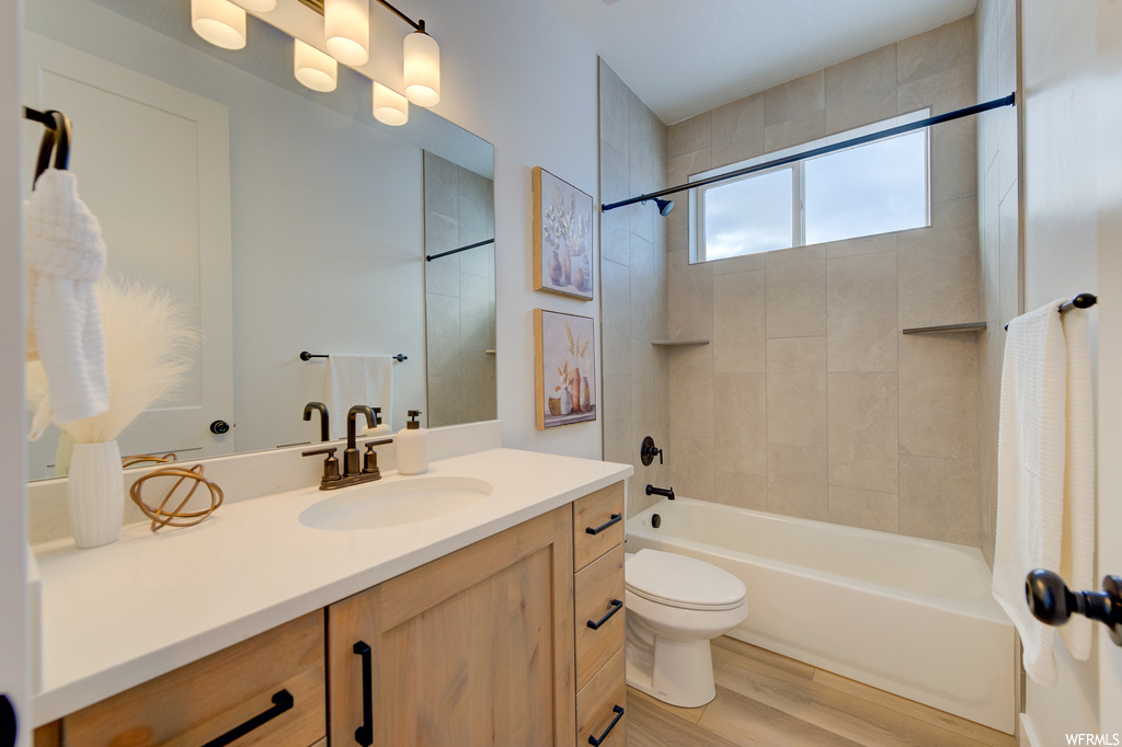 Full bathroom with tiled shower / bath combo, toilet, large vanity, and hardwood / wood-style flooring