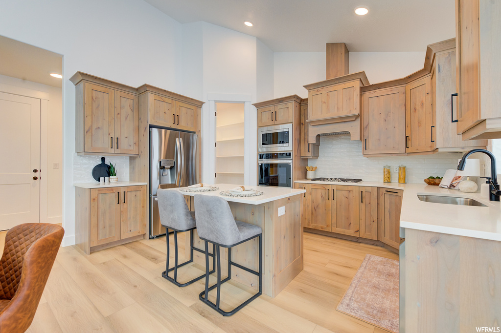 Kitchen with sink, light hardwood / wood-style flooring, stainless steel appliances, a kitchen island, and backsplash