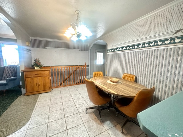 Tiled dining space with a healthy amount of sunlight, a notable chandelier, and crown molding