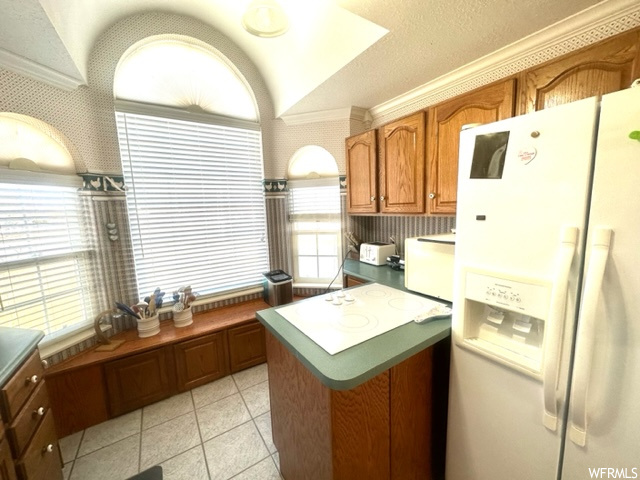Kitchen with ornamental molding, white fridge with ice dispenser, and light tile floors