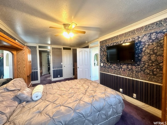 Bedroom with dark carpet, ceiling fan, a textured ceiling, and crown molding